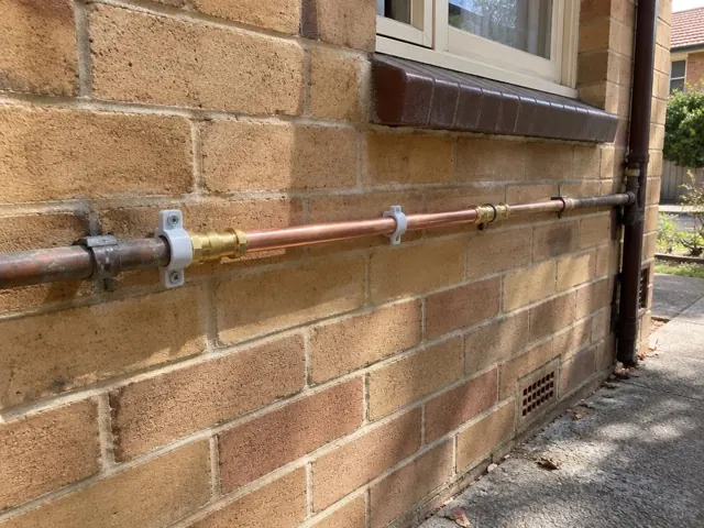 Repaired copper water pipe on a brick exterior wall beneath a window in Harris Park