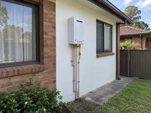 Wall-mounted hot water unit with copper pipes beside a brick and rendered house exterior in Northmead